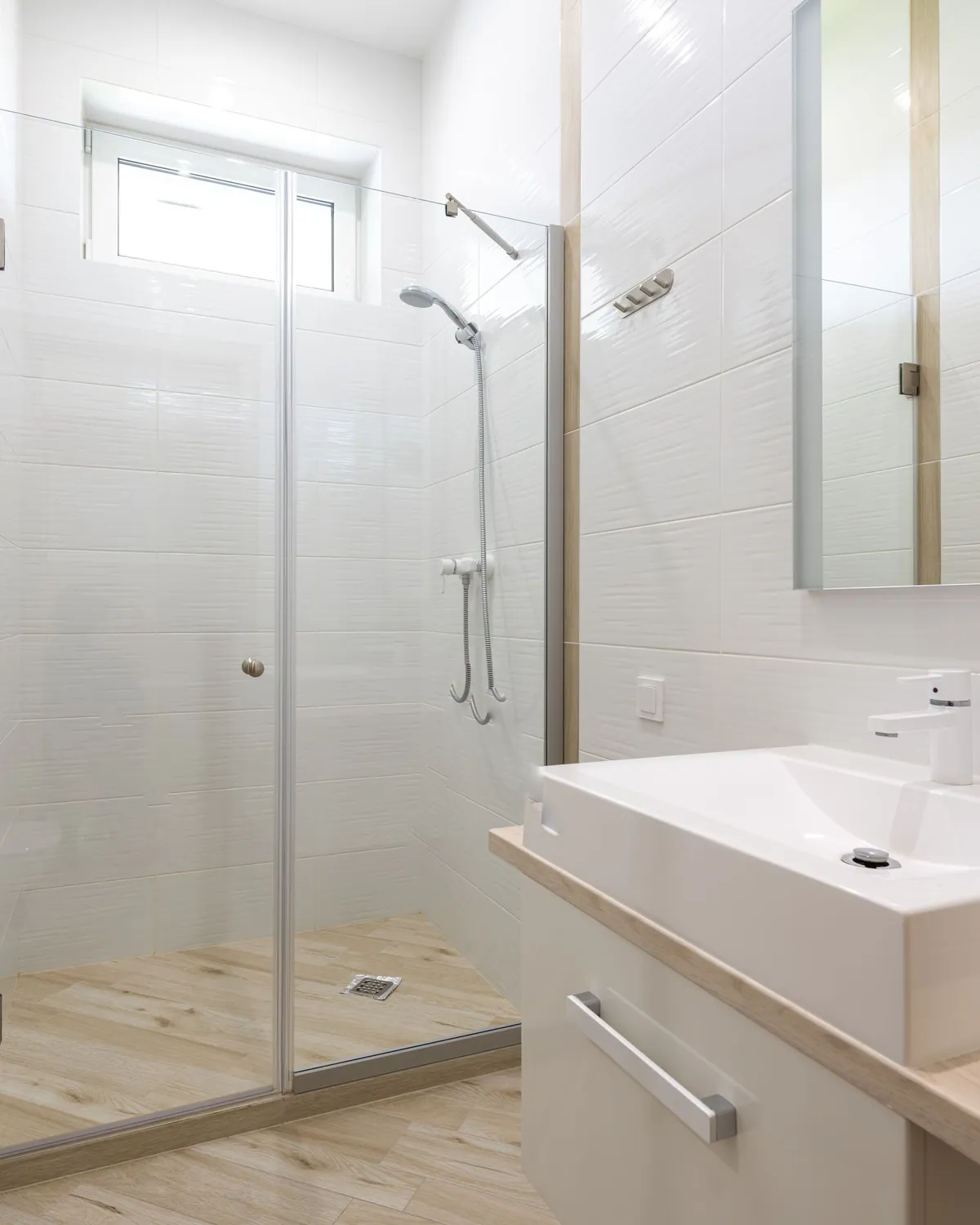 A bright, clean white-tiled bathroom with a glass shower enclosure, for shower mold removal in Falls Church, VA