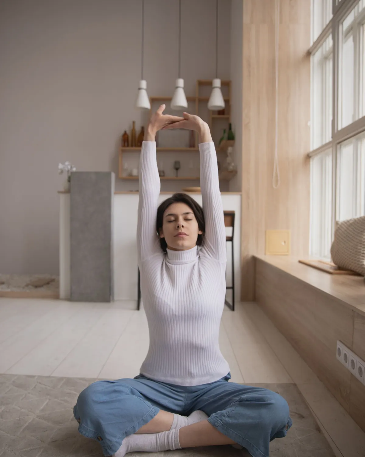 A woman stretching on the floor of a bright room beside a large window, for mold prevention in Falls Church, VA